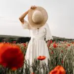 unrecognizable woman with hat standing in meadow with flowers