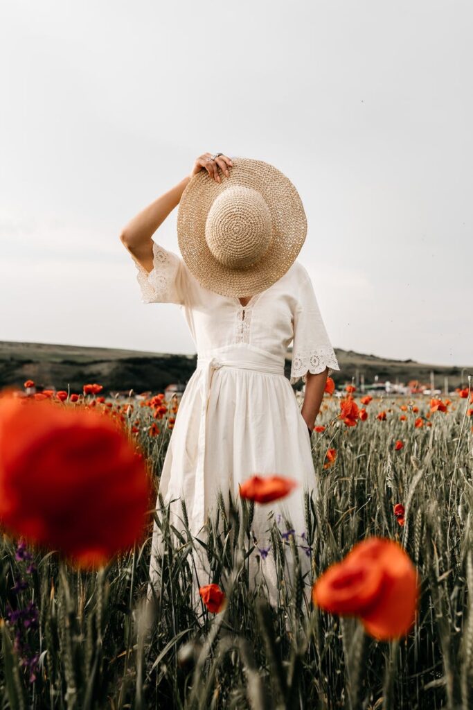 unrecognizable woman with hat standing in meadow with flowers