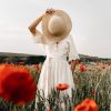 unrecognizable woman with hat standing in meadow with flowers
